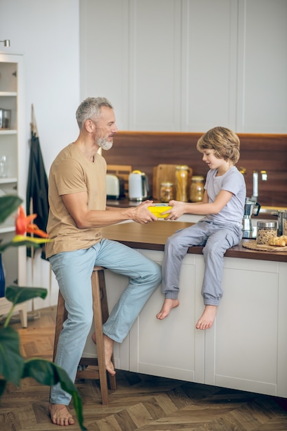 Papà e figlio. Uomo maturo in maglietta beige e suo figlio in cucina a casa