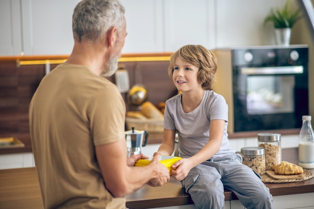 Papà e figlio. Uomo maturo in maglietta beige e suo figlio in cucina a casa