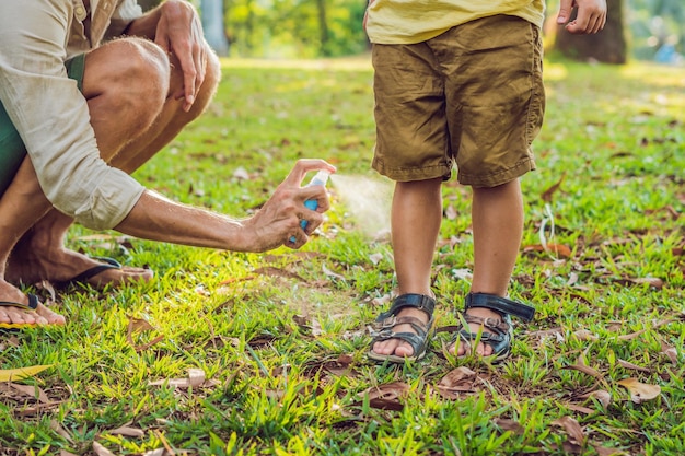 Papà e figlio usano spray antizanzare spruzzando repellente per insetti sulla pelle all'aperto