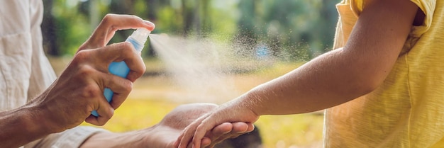 Papà e figlio usano spray per zanzarespruzzando repellente per insetti sulla pelle banner esterno formato lungo