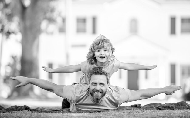 Papà felice che si diverte con il bambino si rilassa insieme sulla relazione con l'erba del parco verde