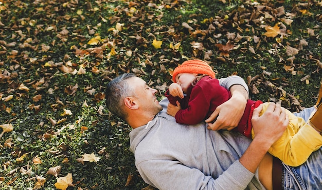 Papà felice gioca con la sua piccola figlia nel parco sulle foglie d'autunno la solleva in alto tra le sue braccia