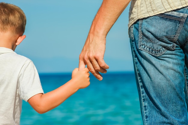 Papà felice tiene la mano di un bambino in riva al mare greco nella natura