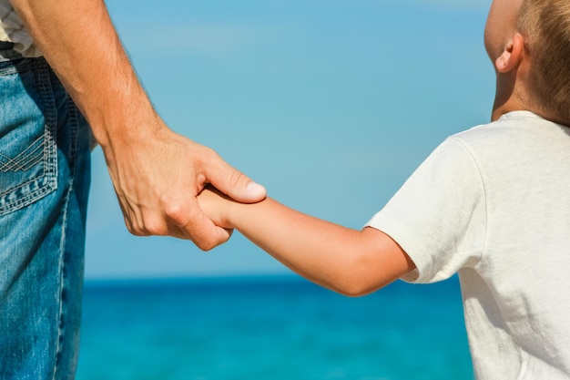 Papà felice tiene la mano di un bambino in riva al mare greco nella natura