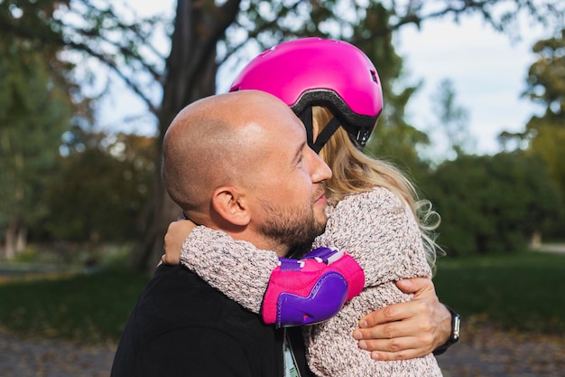 Papà gioioso e figlia piccola in un casco che si abbracciano nel parco