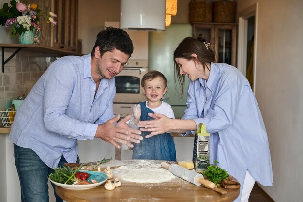 Papà mamma e figlia cucinano insieme la pizza in cucina T