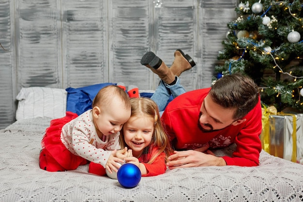 Papà sul letto con le sue figlie sullo sfondo dell'albero di Natale