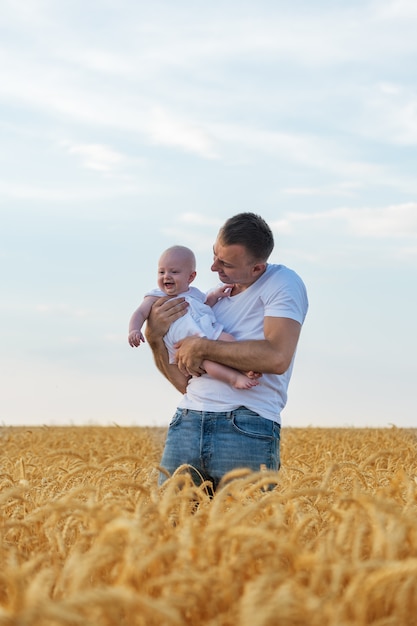 Papà tiene il bambino sul campo spaziale di grano e cielo maturi. Telaio verticale