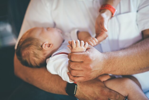 Papà tiene in braccio il suo simpatico neonato con le mani in camicie bianche