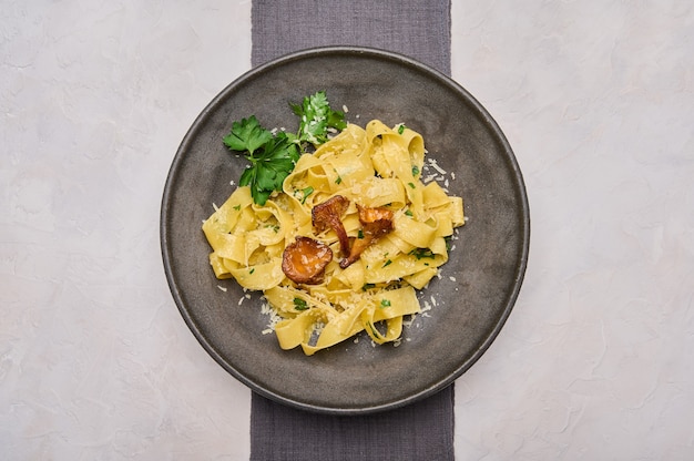 Pappardelle di pasta italiana con funghi finferli formaggio e prezzemolo su piatto scuro e tovagliolo