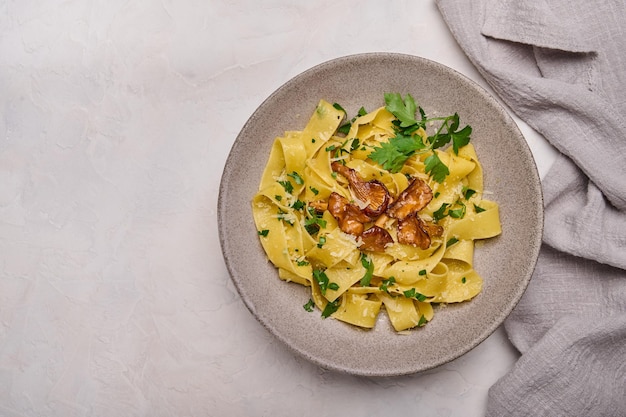 Pappardelle di pasta piatta con funghi finferli formaggio e prezzemolo su piatto grigio con tovagliolo