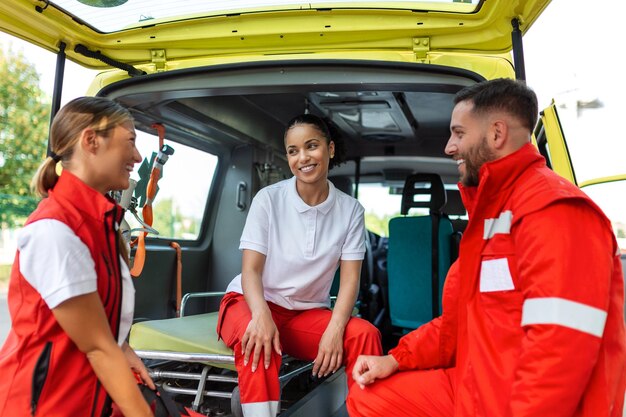 Paramedico e dottore in piedi sul lato dell'ambulanza Il dottore sta portando una borsa per traumi medici Un gruppo di tre paramedici in piedi davanti all'ambulanza con un sorriso