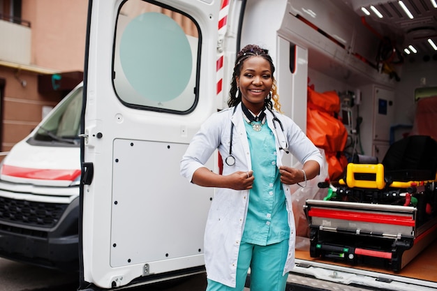 Paramedico femminile afroamericano in piedi davanti all'auto dell'ambulanza.