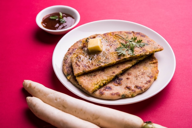 Paratha ripiena di daikon o ravanello o mooli servita in un piatto con burro e ketchup, su sfondo colorato o in legno. messa a fuoco selettiva