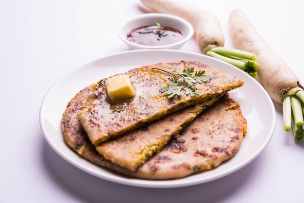 Paratha ripiena di daikon o ravanello o mooli servita in un piatto con burro e ketchup, su sfondo colorato o in legno. messa a fuoco selettiva