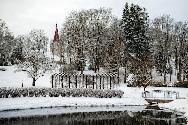 Parco cittadino con ponte stagno e chiesa sullo sfondo in una giornata invernale nevosa Kandava