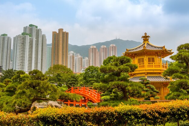 Parco di Hong Kong. Padiglione d'oro circondato da piante e alberi. Grattacieli e montagne sullo sfondo