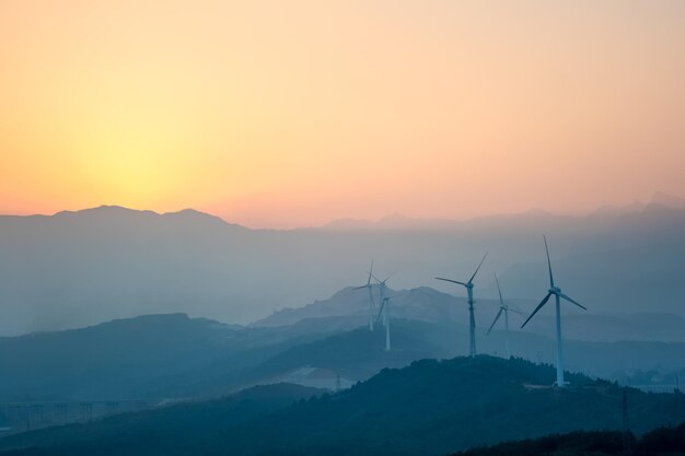 Parco eolico con silhouette di montagne lontane al tramontoxAxA