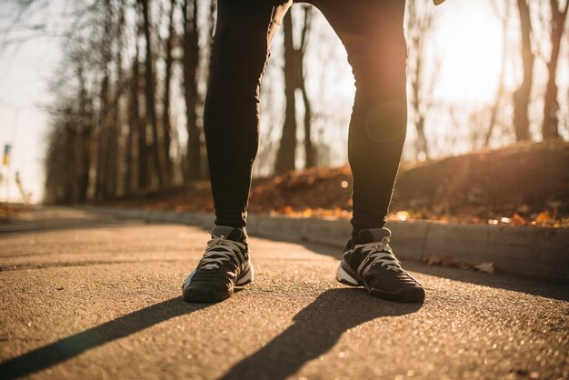 Pareggiatore maschio gambe, allenamento mattutino all'aperto. Corridore in abbigliamento sportivo in allenamento nel parco