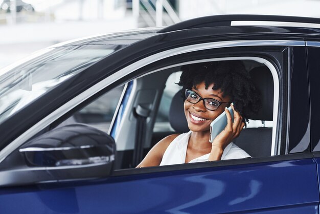 Parla al telefono. La giovane donna afroamericana si siede all'interno della nuova automobile moderna.