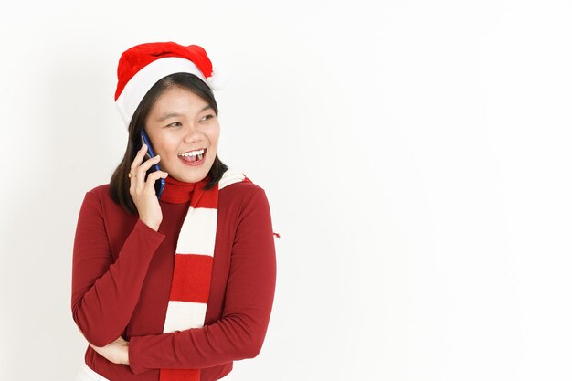 Parlando al telefono con l'espressione felice del viso di una donna asiatica che indossa un dolcevita rosso e un cappello da Babbo Natale