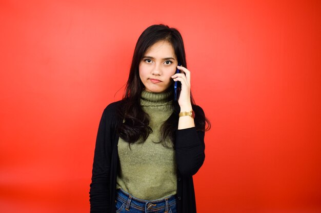 Parlando al telefono di giovani belle donne asiatiche che usano un maglione nero con sfondo rosso isolato