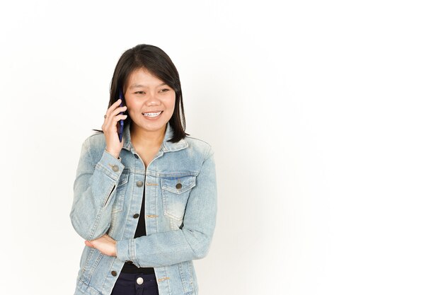 Parlando al telefono di una bella donna asiatica che indossa giacca di jeans e camicia nera isolata su bianco