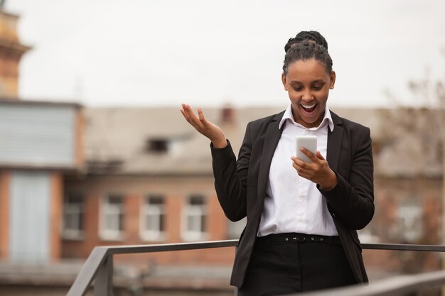 Parlando al telefono stupita donna d'affari afroamericana in abbigliamento da ufficio sorridente