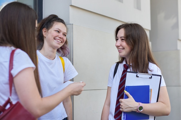 Parlando di studentesse. Tre adolescenti con libri di zaini, risate e discorsi all'aperto.