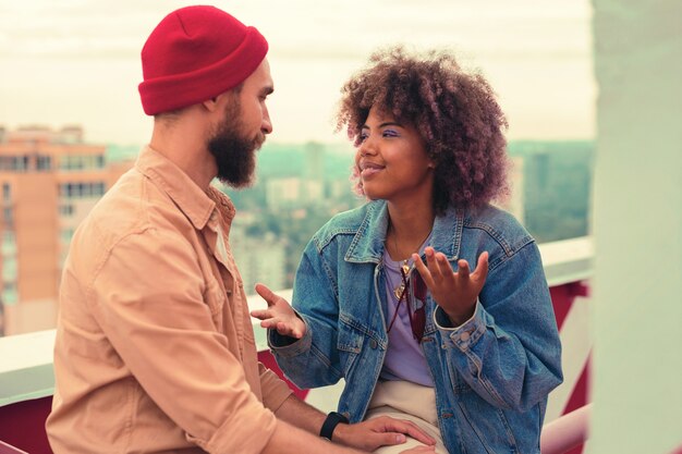 Parlando. Giovane ragazza espressiva che sorride e che usa i gesti mentre guarda il suo amato uomo e parla con lui