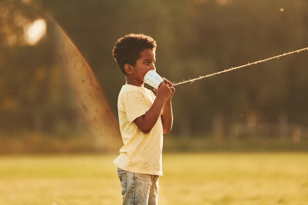 Parlando usando la tazza sul nodo Il bambino afroamericano si diverte sul campo durante il giorno d'estate