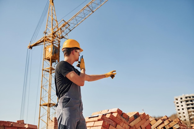 Parlare per telefono Operaio edile in uniforme e equipaggiamento di sicurezza ha un lavoro sulla costruzione