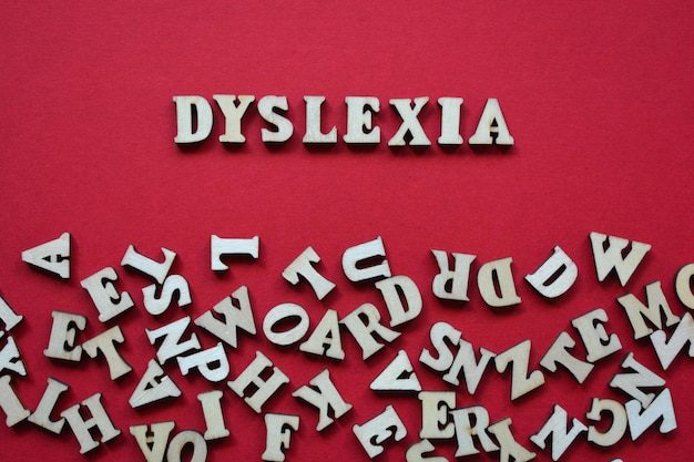 Parola di dislessia in lettere dell'alfabeto di legno circondate da lettere casuali su sfondo rosso