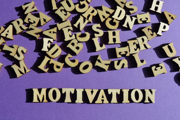 Parola di motivazione e lettere casuali dell'alfabeto di legno su sfondo viola