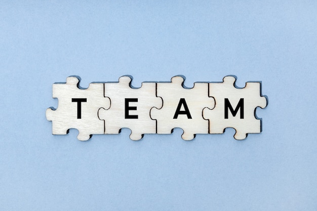 Parola di squadra su pezzi di puzzle in legno isolati su sfondo blu. Vista dall'alto