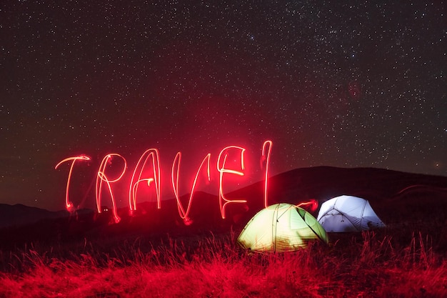 Parola di viaggio al neon rosso Due tende illuminate sotto le stelle in montagna di notte