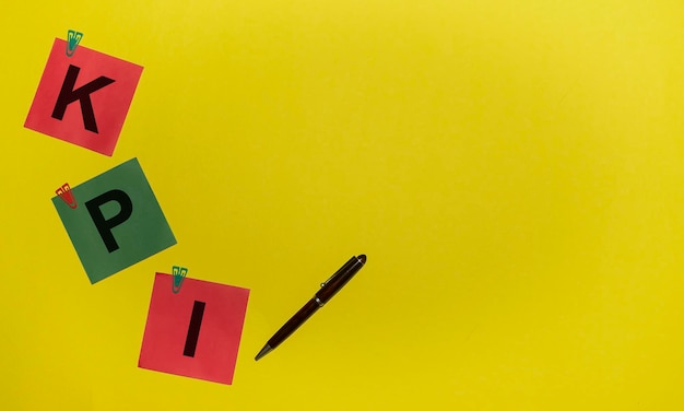 Parola KPI su adesivi verdi e rossi con clip e penna su sfondo giallo con spazio per la copia