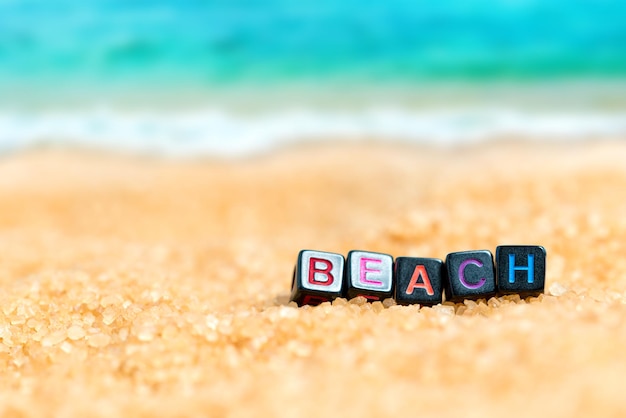 Parola multicolore SPIAGGIA da cubi neri nella sabbia sullo sfondo della spiaggia e del mare