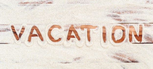 Parola vacanza scritta dalla sabbia sulle assi di legno
