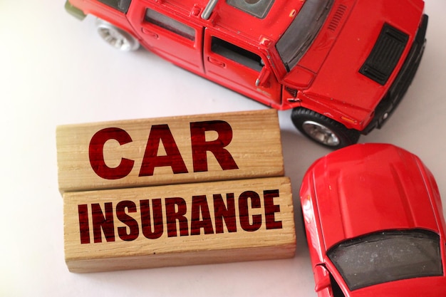 Parole di assicurazione auto su blocchi di legno e due auto rosse in incidente stradale su sfondo bianco Concetto di assicurazione