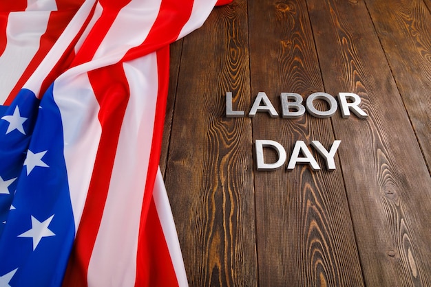 Parole festa del lavoro posate con lettere in metallo argentato su superficie di legno con bandiera USA stropicciata sul lato sinistro