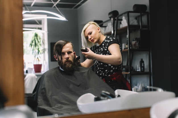 Parrucchiere alla moda taglio dei capelli del cliente al negozio di barbiere.