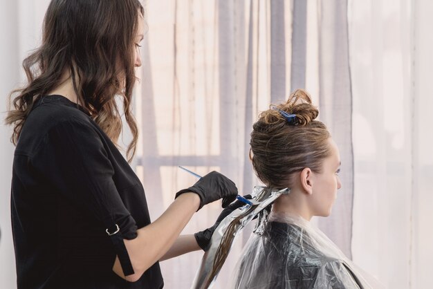 Parrucchiere che colora i capelli della giovane donna facendo uso di stagnola