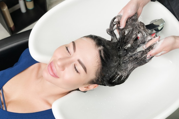 Parrucchiere che lavora con la donna castana di fascino nel salone di capelli professionale.