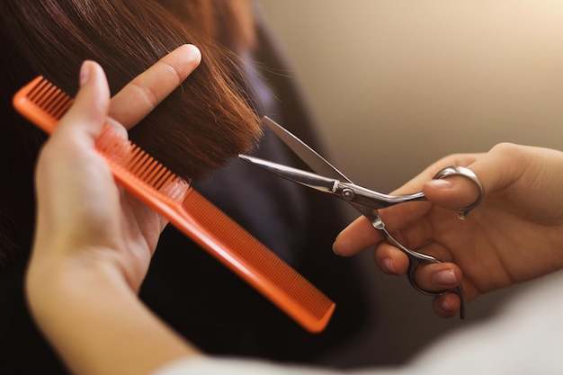 Parrucchiere che taglia i capelli castani con le forbici nel salone di bellezza, primo piano