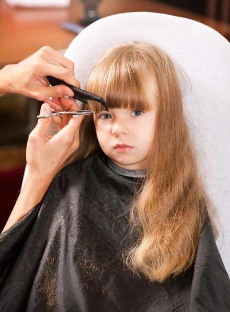 Parrucchiere che taglia i capelli di una bambina bionda