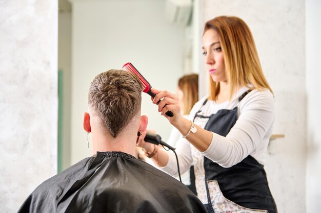 Parrucchiere che taglia i capelli e acconcia un cliente nel negozio di barbiere