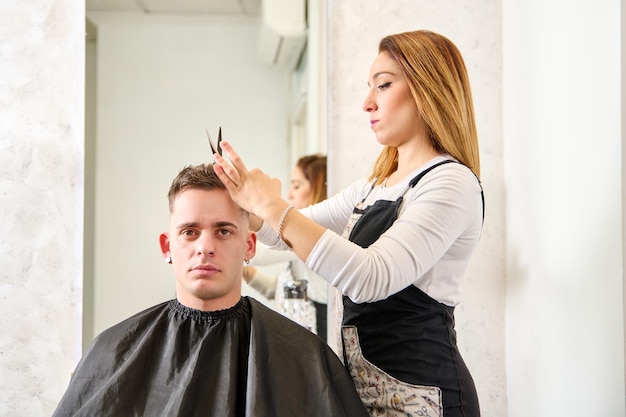 Parrucchiere che taglia i capelli e acconcia un cliente nel negozio di barbiere