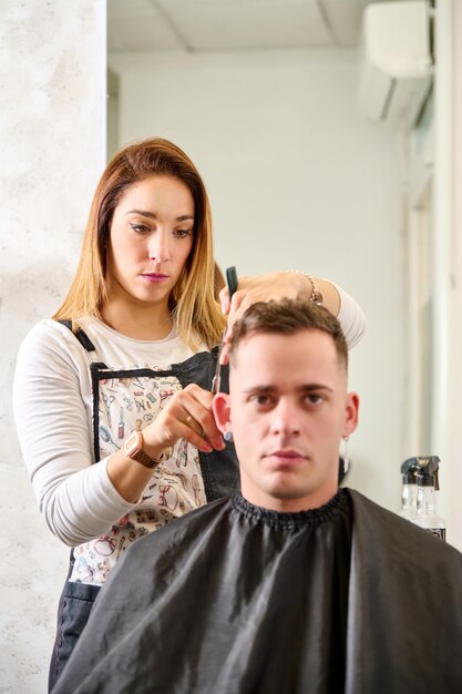 Parrucchiere che taglia i capelli e acconcia un cliente nel negozio di barbiere