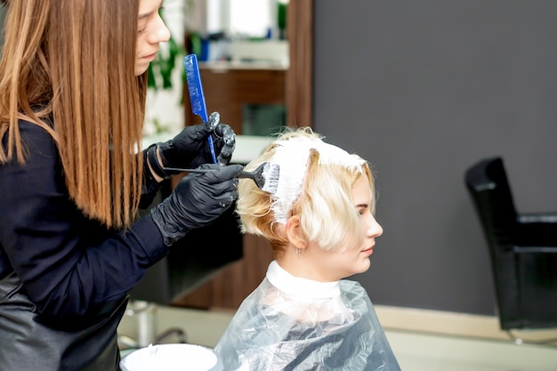 Parrucchiere che tinge i capelli della donna in colore bianco al salone di bellezza.